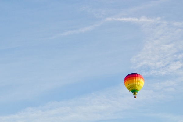 A rainbow-colored hot air balloon against a pale blue sky in Belgium
