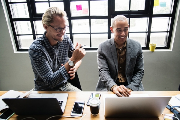 two men sitting beside each other in front of laptops