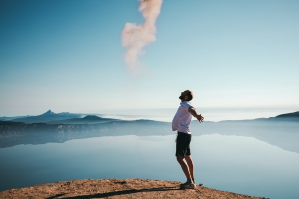 man standing on sand while spreading arms beside calm body of water