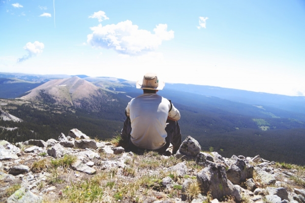 person sitting on a gray rock watching over a mountain