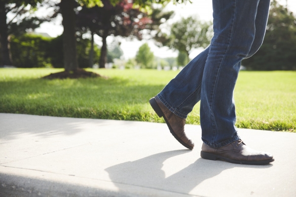 person wearing pair of pown shoes and blue denim jeans walking on concrete ground near green grass field during daytime