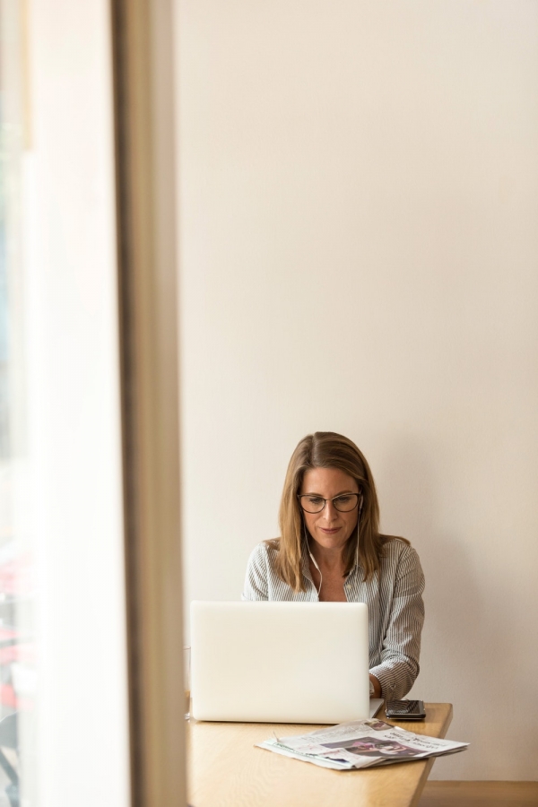 woman wearing grey striped dress shirt sitting down near pown wooden table in front of white laptop computer