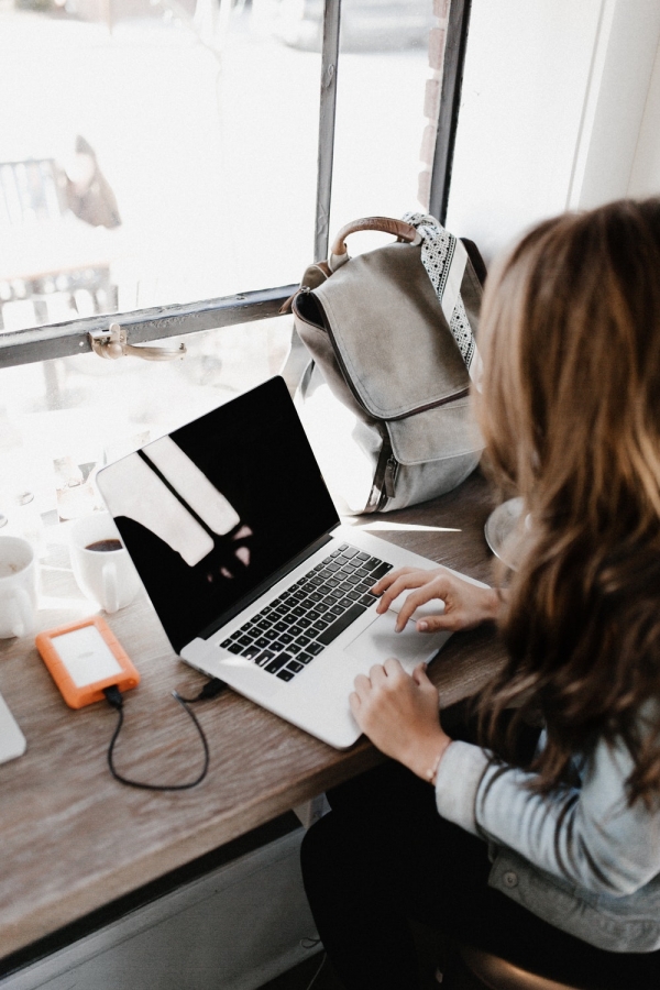 girl wearing grey long-sleeved shirt using MacBook Pro on pown wooden table