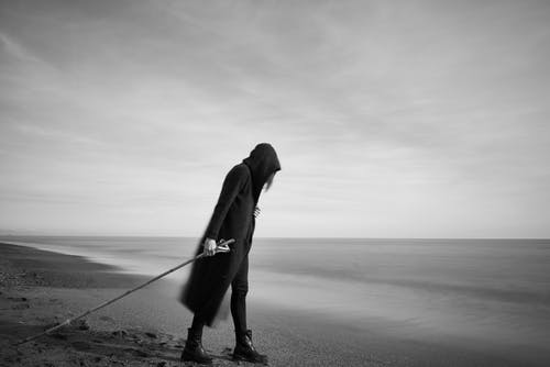Woman in Black Cloak With Fishing Pole Standing in Beach